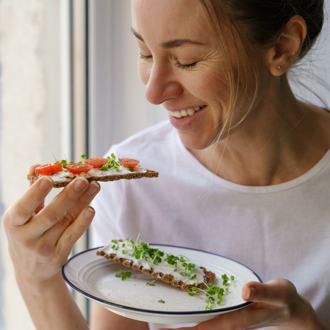 Woman about to eat a cracker with cream cheese, tomatoes and microgreens sprinked on top